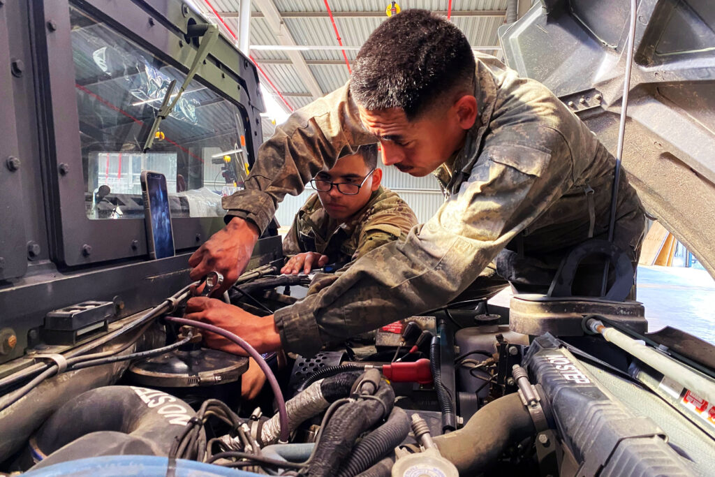 a couple of soldiers working on a car engine.